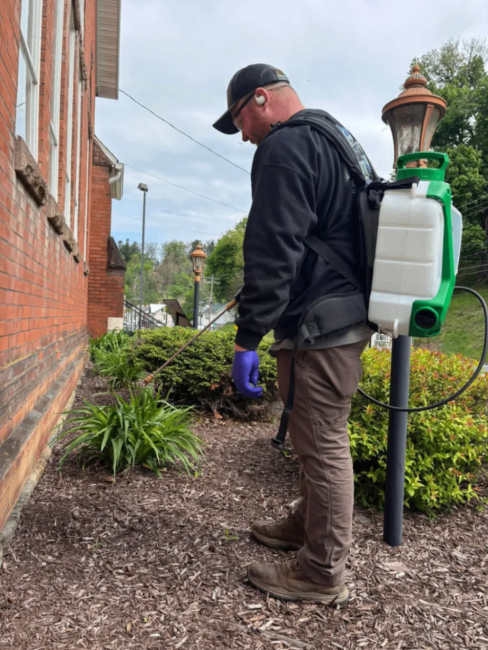 Andrew, a Pest Shark technician, treating the landscaping beside a brick home
